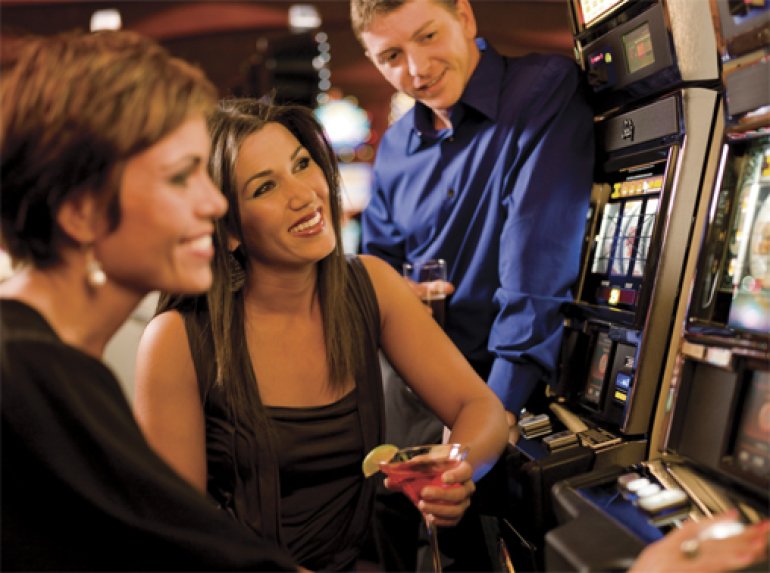 Una ragazza è seduta alla slot machine e i suoi amici la osservano mentre gioca.
